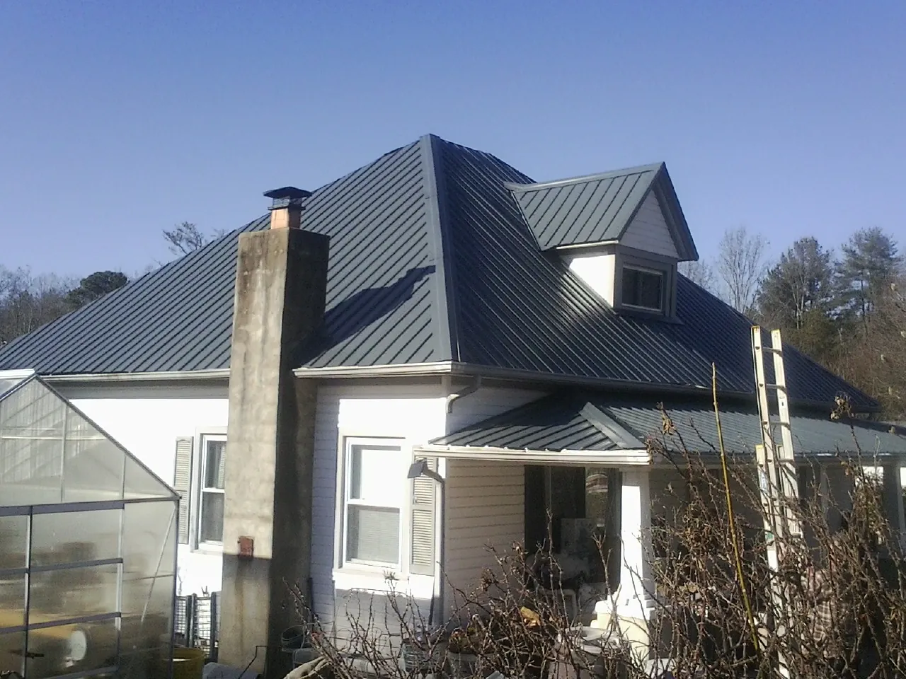 Dark blue standing seam metal roof on a white farmhouse with dormer — Slate & Tile Roof Repair by Roofing Brothers in Eustis