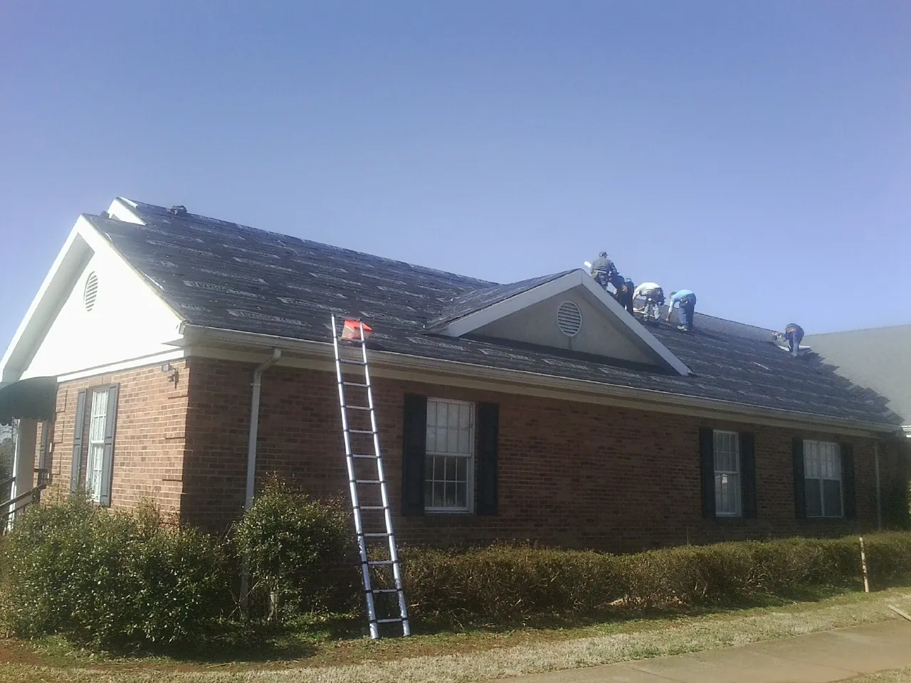 Crew tearing shingles off a brick ranch roof with a ladder set — Emergency Roof Repair work by our crew in Eustis