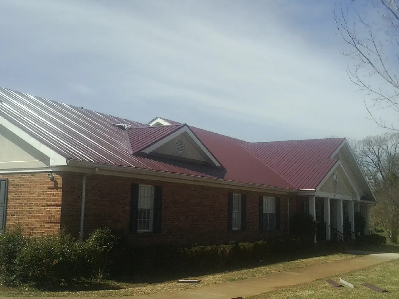 Red metal roof with gabled entries on a long brick building, from a Hail Damage Roof Repair job in Eustis