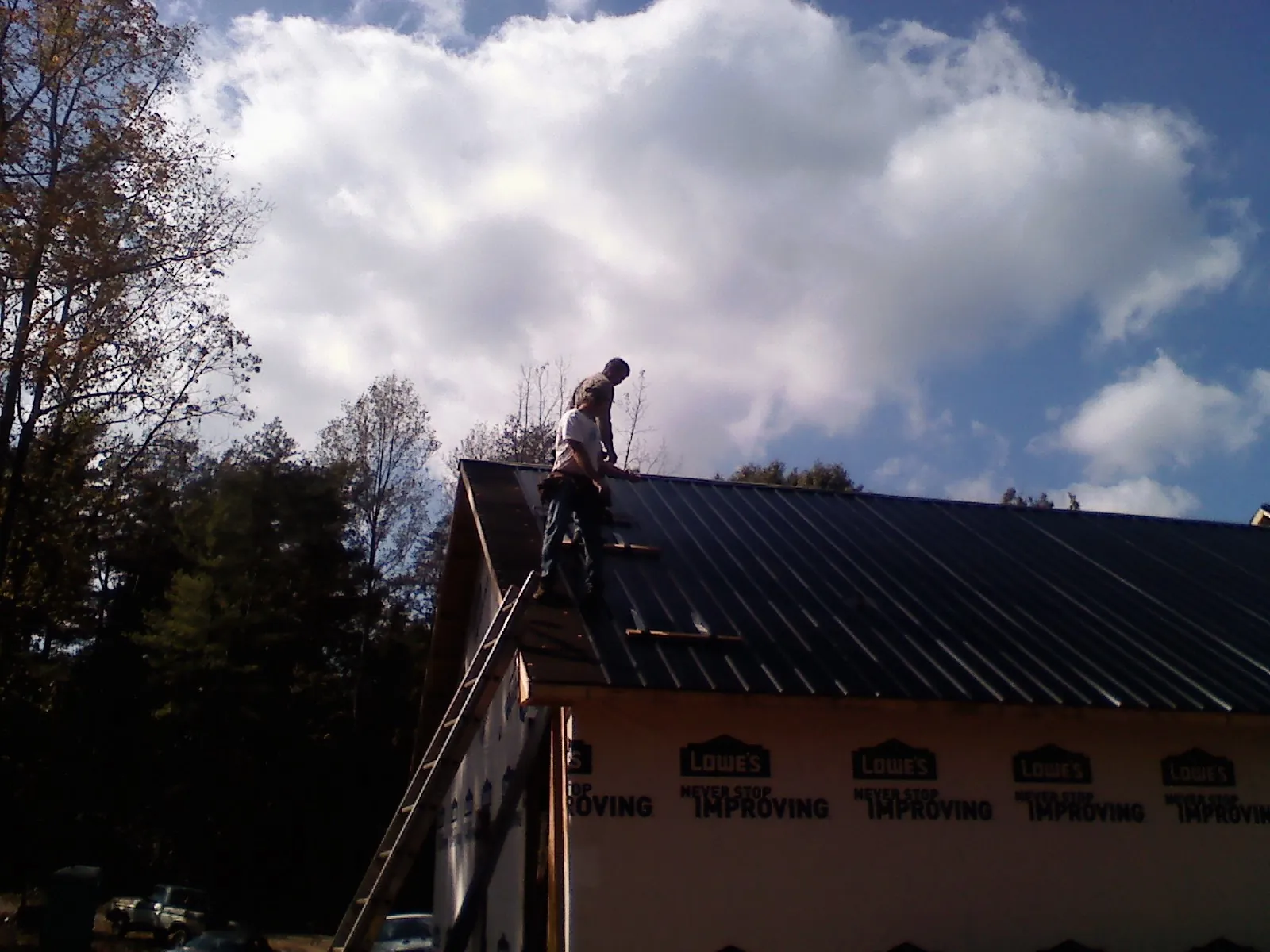 Roofer fastening dark metal panels high against a cloudy sky, from a Roof Inspection job in Eustis